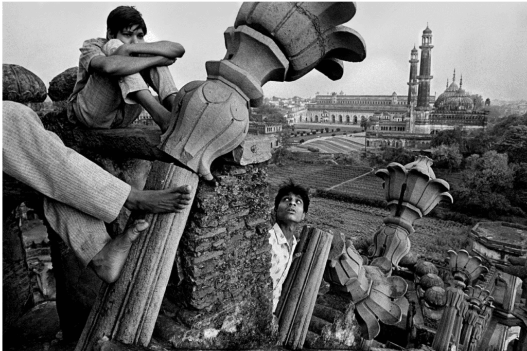 In this black and white photo, a man's eyes wider at a crumbling cement pillar seemingly falling towards him. 