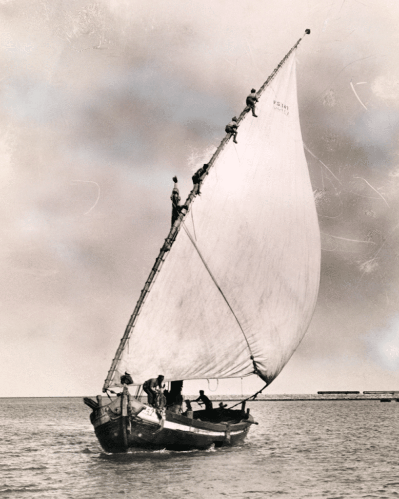 In this back and white photo, a man scales a tall mast of a sailboat. 